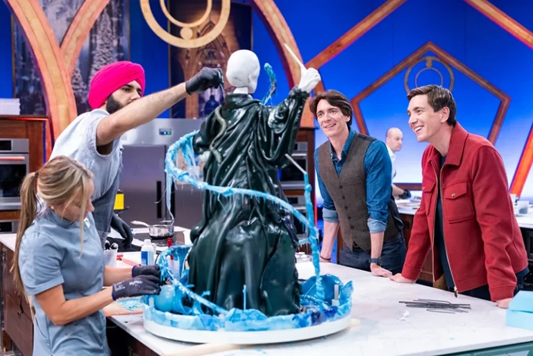 This image released by Food Network shows hosts Oliver Phelps, right, and James Phelps, watching contestants Katie Bonzer, left, and Jujhar Mann on the set of the competition series “Harry Potter: Wizards of Baking.” (Anders Krusberg/Food Network via AP)