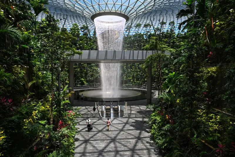 People walk past the Rain Vortex indoor waterfall feature at Jewel Changi Airport in Singapore on August 19, 2021. (Photo by Roslan RAHMAN / AFP) (Photo by ROSLAN RAHMAN/AFP via Getty Images)