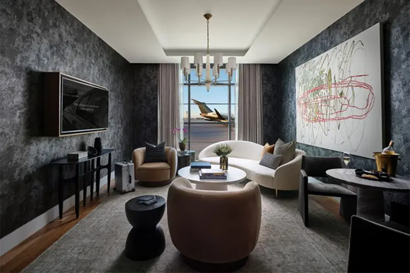 Modern airport sanctuary featuring textured dark walls, plush seating, and abstract art, overlooking the tarmac.
