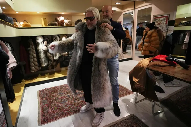 Sales manager for Pajaro, a luxury Italian fashion brand, Marco Molinari, right, helps his client, Stefano Vannicola, put on a fur coat in Cortina d’Ampezzo, Italy, Saturday, Feb. 14, 2026. (AP Photo/Alessandra Tarantino)