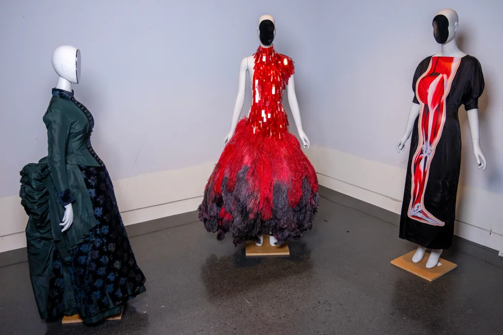 A vintage walking dress, from left, an Alexander McQueen dress, and a Christopher Kane dress are held in preparation for The Metropolitan Museum of Art’s spring exhibition, “Costume Art,” on Thursday, Feb. 12, 2026, in New York. (Photo by Charles Sykes/Invision/AP)