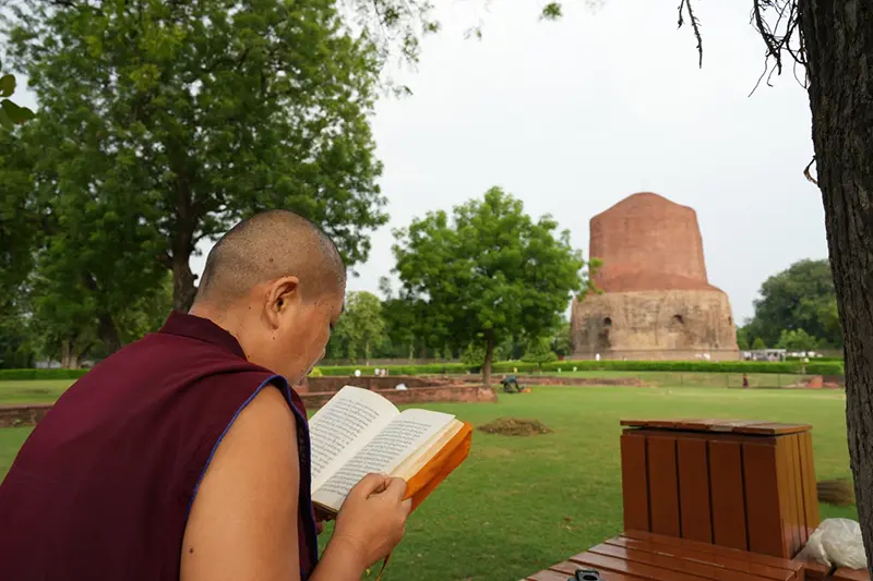 A Buddhist devout reads in front of Dhamek Stupa in the ancient Buddhist site of Sarnath, India, Saturday, July 18, 2026. (AP Photo/Rajesh Kumar Singh)