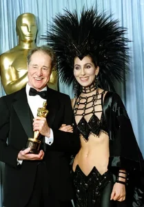 Actor-singer Cher wears a creation by designer Bob Mackie as she poses with actor Don Ameche after presenting him with the Oscar for best supporting actor at the Academy Awards in Los Angeles, March 24, 1986. (AP Photo/Lennox McLendon, File)